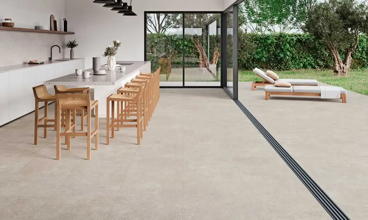 Cocina moderna con isla y taburetes, conectada a terraza con tumbonas. Un proyecto llave en mano que fusiona interior y exterior.
