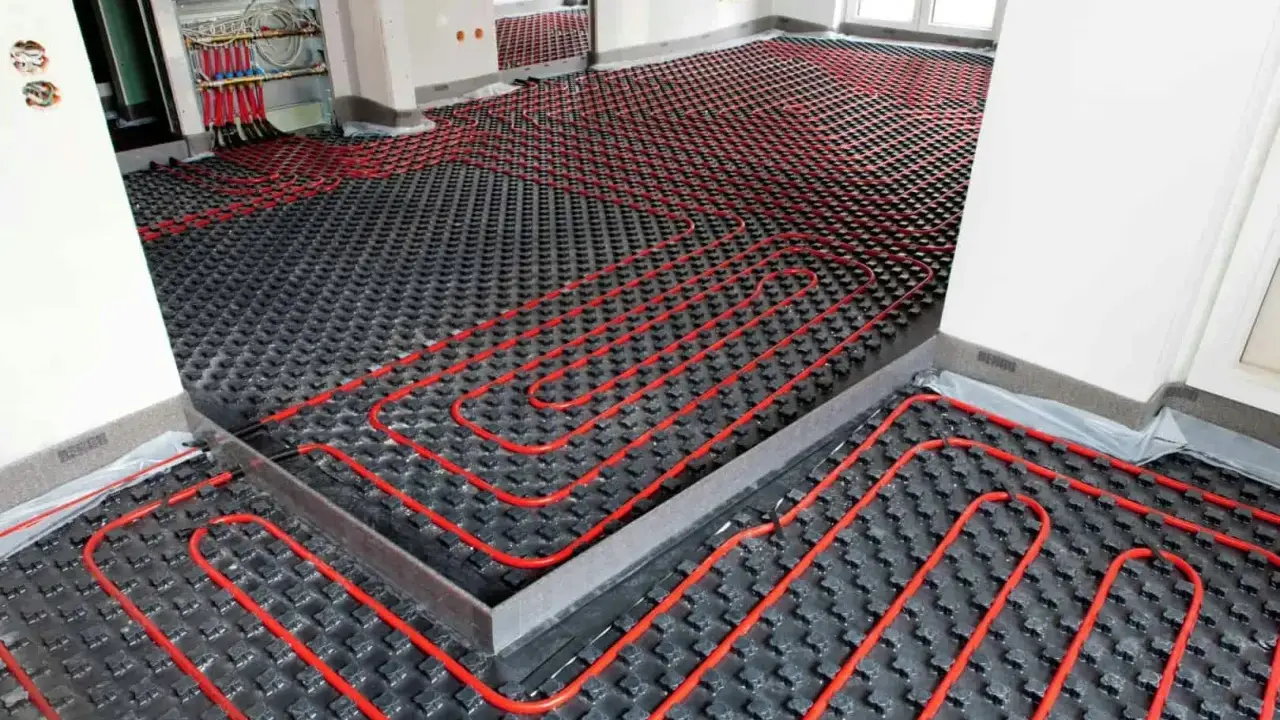 Instalación de un sistema de calefacción por suelo radiante enfria. Tubos rojos serpentean sobre paneles negros en una habitación en construcción.