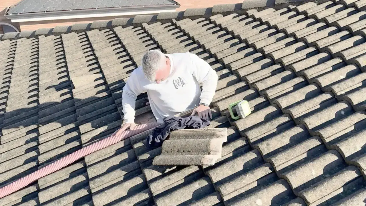 Hombre en tejado trabajando en el aislamiento térmico del tejado. Se ve una manguera rosa y una herramienta verde.