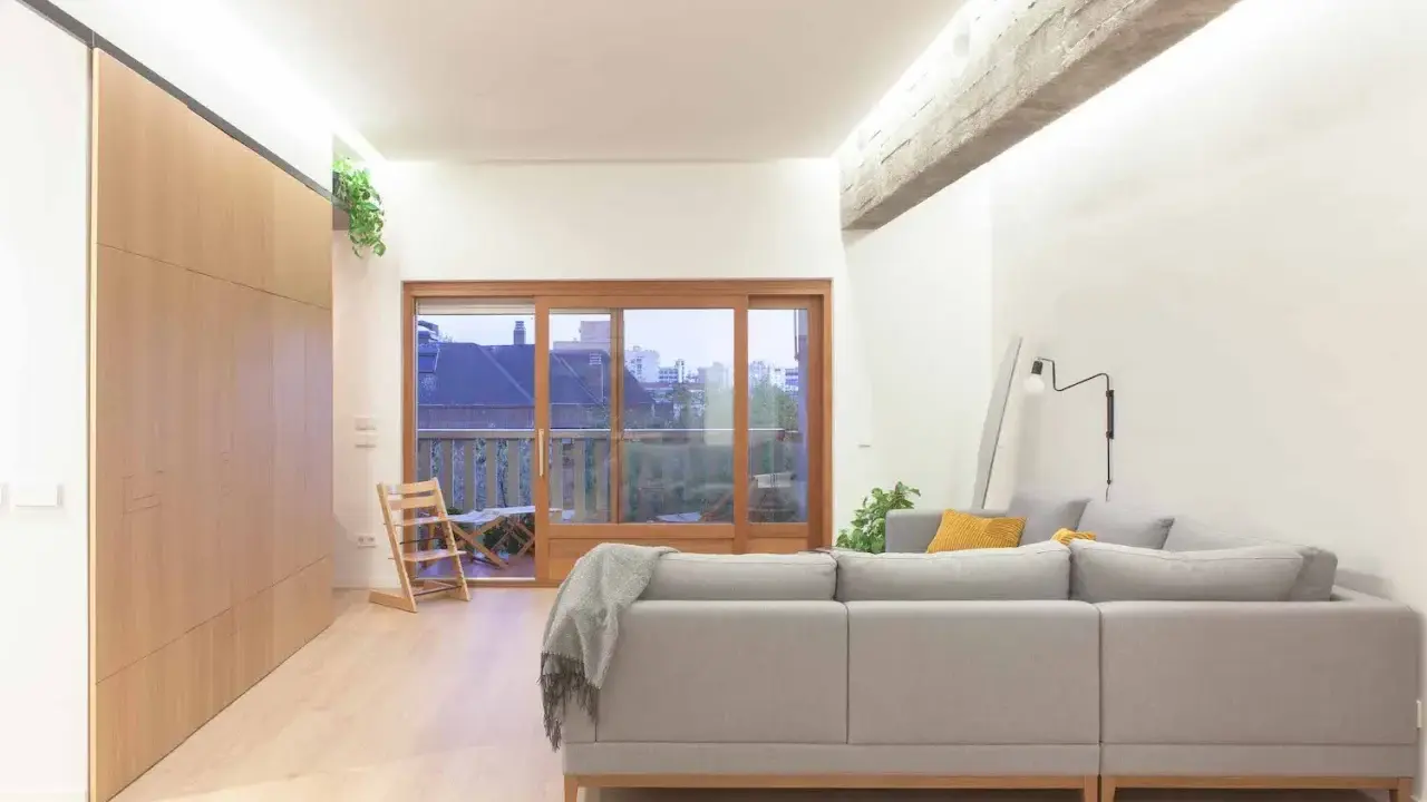 Salón moderno con sofá gris, grandes ventanales y **techos con vigas de hormigón decorar** el espacio con estilo industrial.