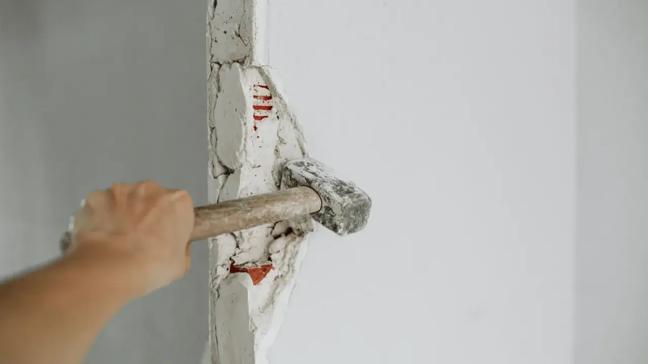Mano golpeando un tabique con un martillo. La pregunta de cuanto se tarda en tirar un tabique depende de la habilidad y el material.