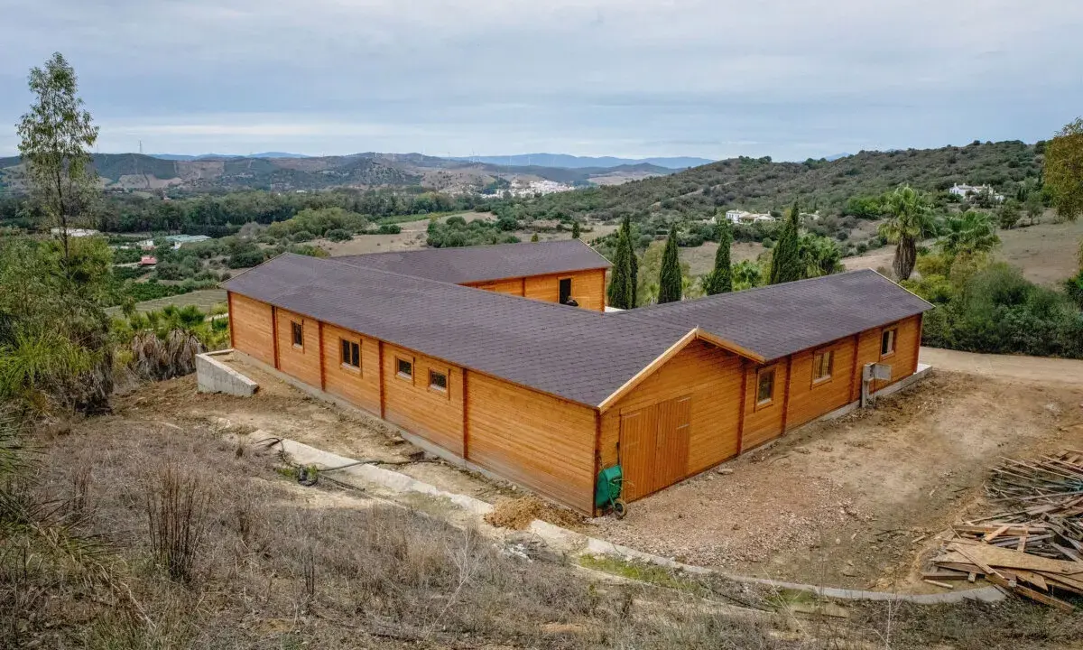 Edificio de madera en forma de L, con tejado oscuro, en un paisaje rural. Ideal para saber cuántos metros cuadrados se pueden construir sin proyecto.