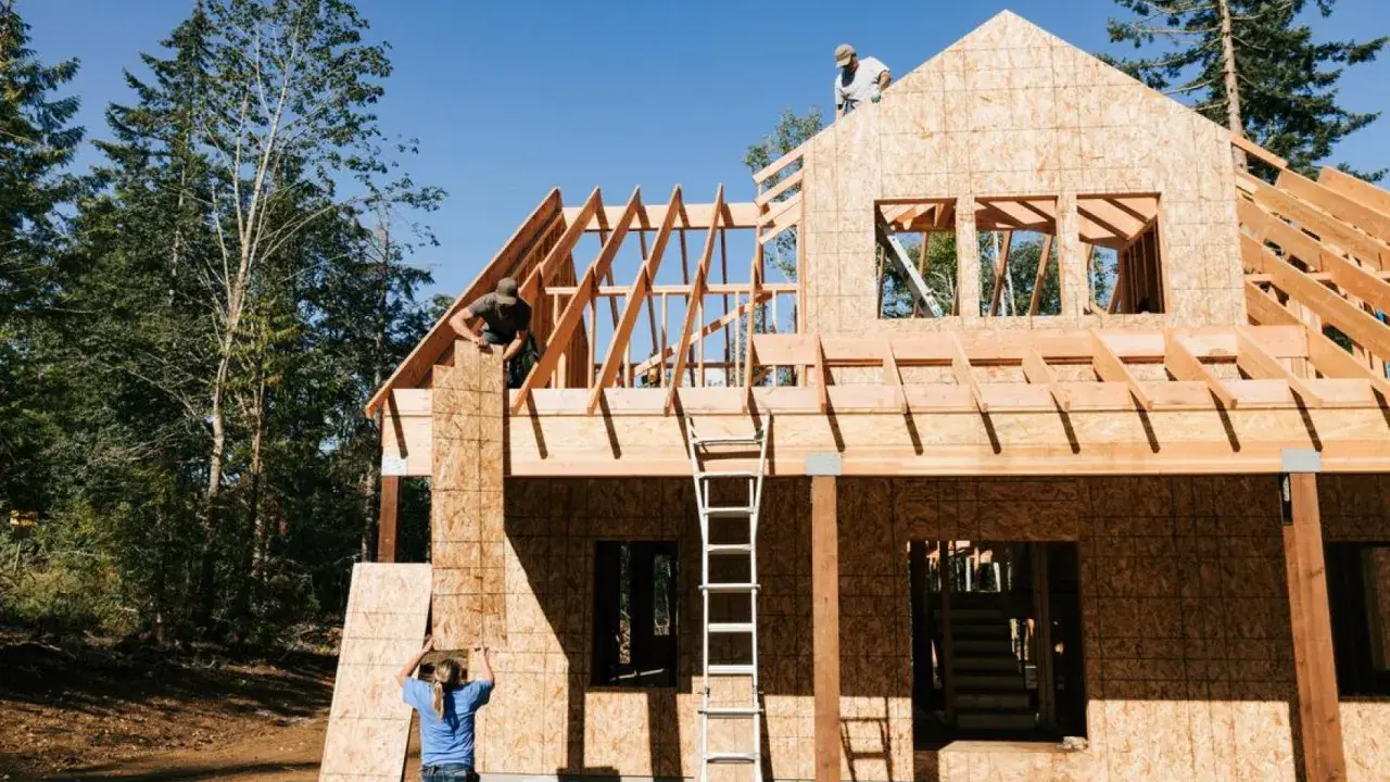 Obreros trabajan en la estructura de madera de una casa, mostrando los pasos a seguir para construir una casa.