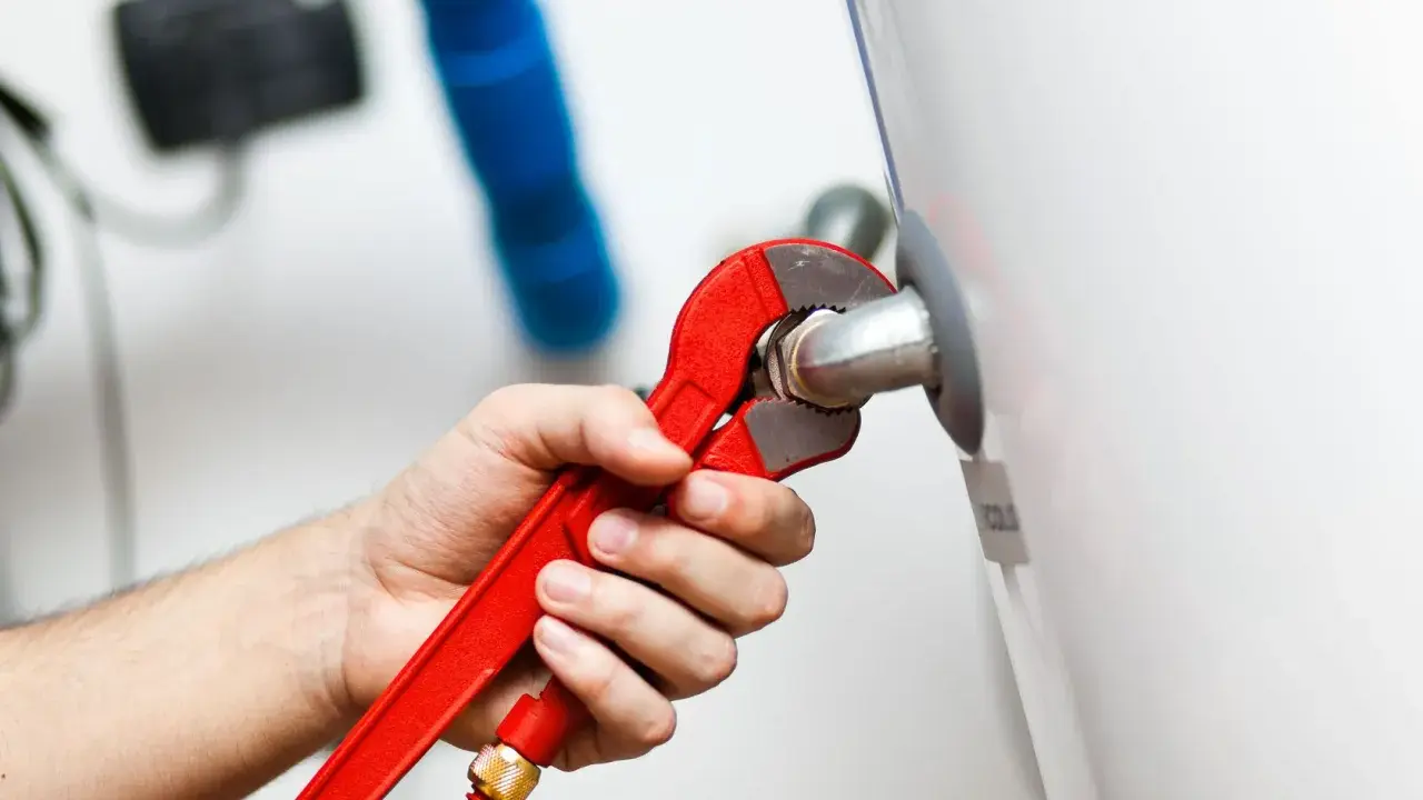 Mano con llave roja ajustando tubería. Es parte de la revisión caldera gas obligatoria para garantizar seguridad y eficiencia.