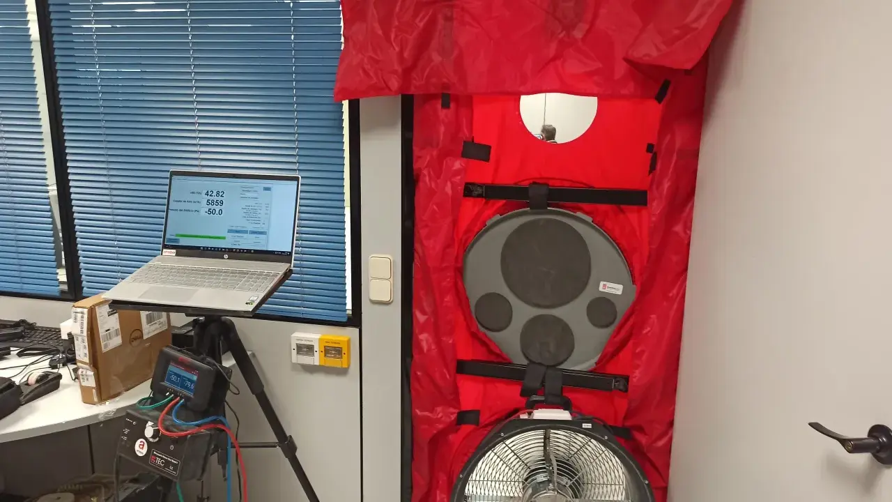 Equipo para blower door test en puerta, con laptop mostrando datos y medidor de presión.