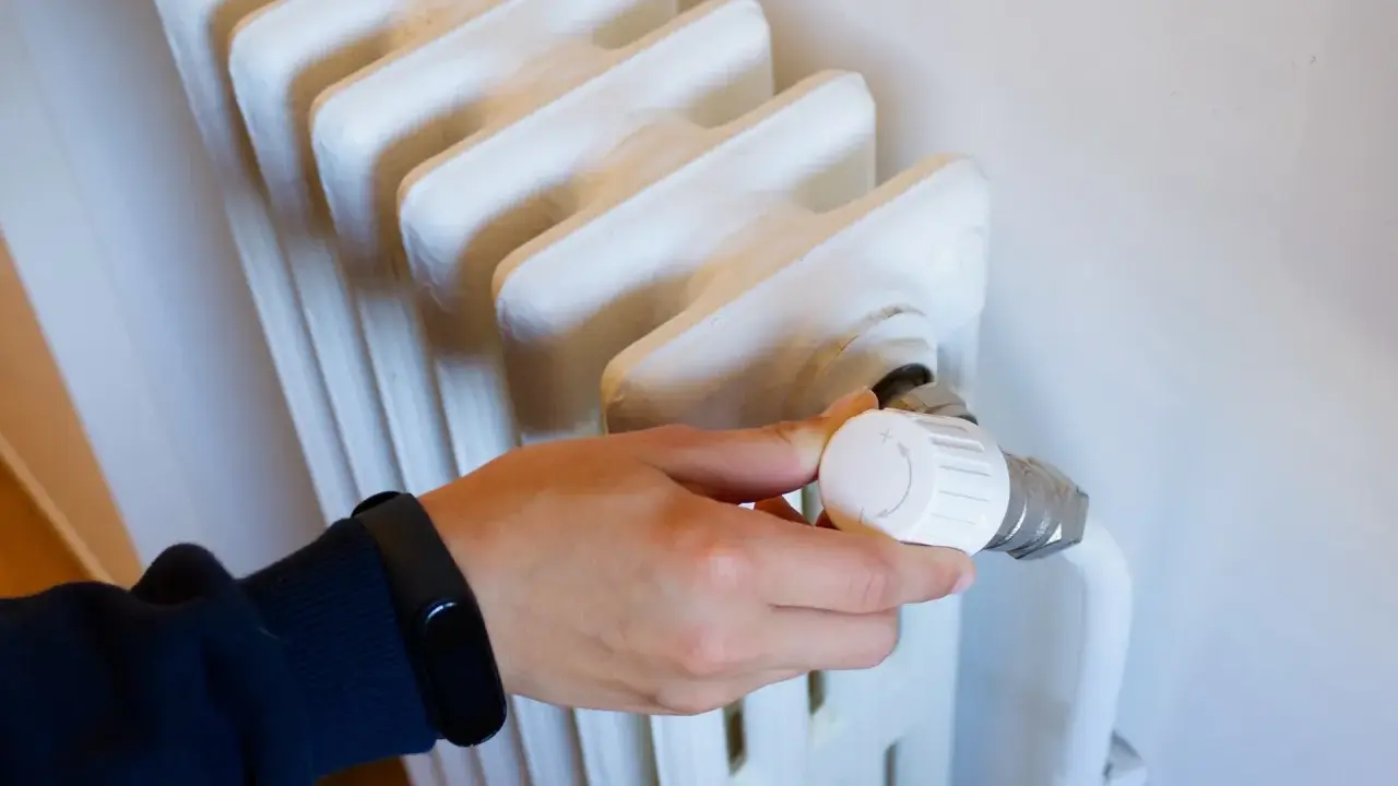 Mano ajustando el termostato de un radiador, parte de los contadores individuales de calefacción central.