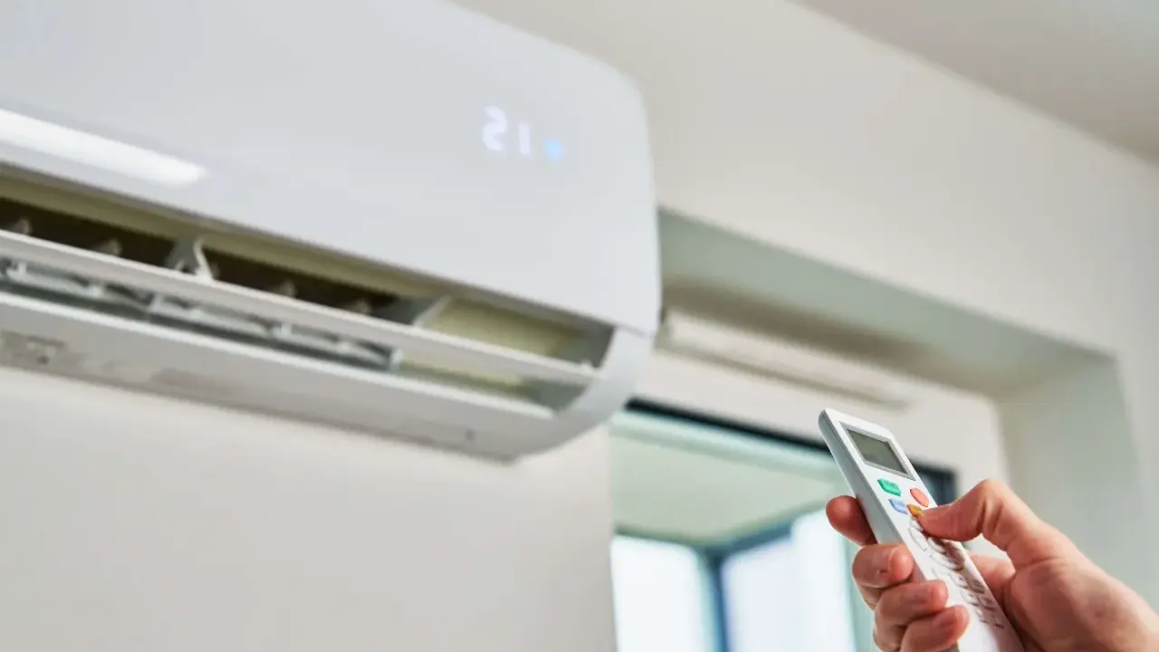 Mano ajustando el control remoto de un aire acondicionado para que gasta menos. La pantalla muestra 21 grados.