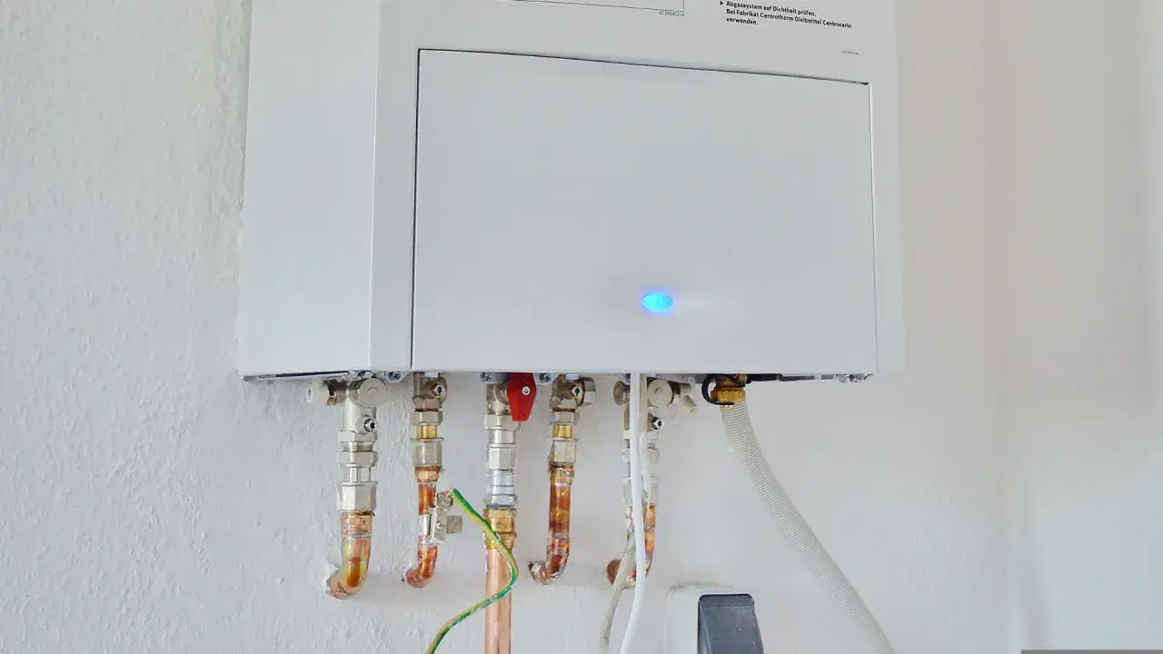 Calentador atmosférico blanco montado en pared con tuberías de cobre y conexiones. Una luz azul parpadea en la unidad, indicando que se puede instalar un calentador atmosférico en el interior.