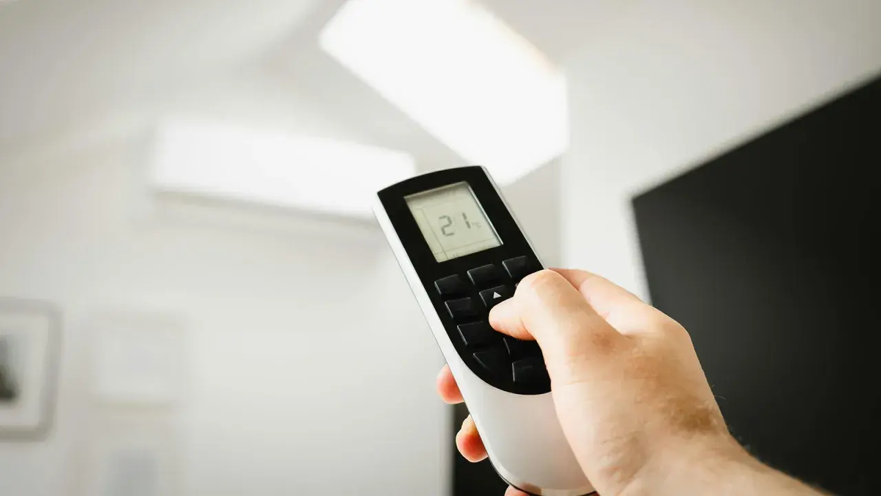 Mano ajustando el mando de aire acondicionado a 21 grados. Instrucciones claras para un confort óptimo.