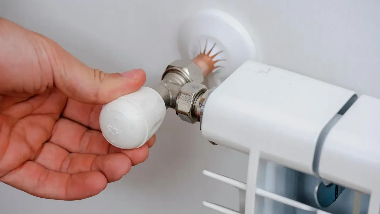 Mano ajustando la perilla de un radiador, mostrando partes de un radiador de agua como la válvula y la conexión.