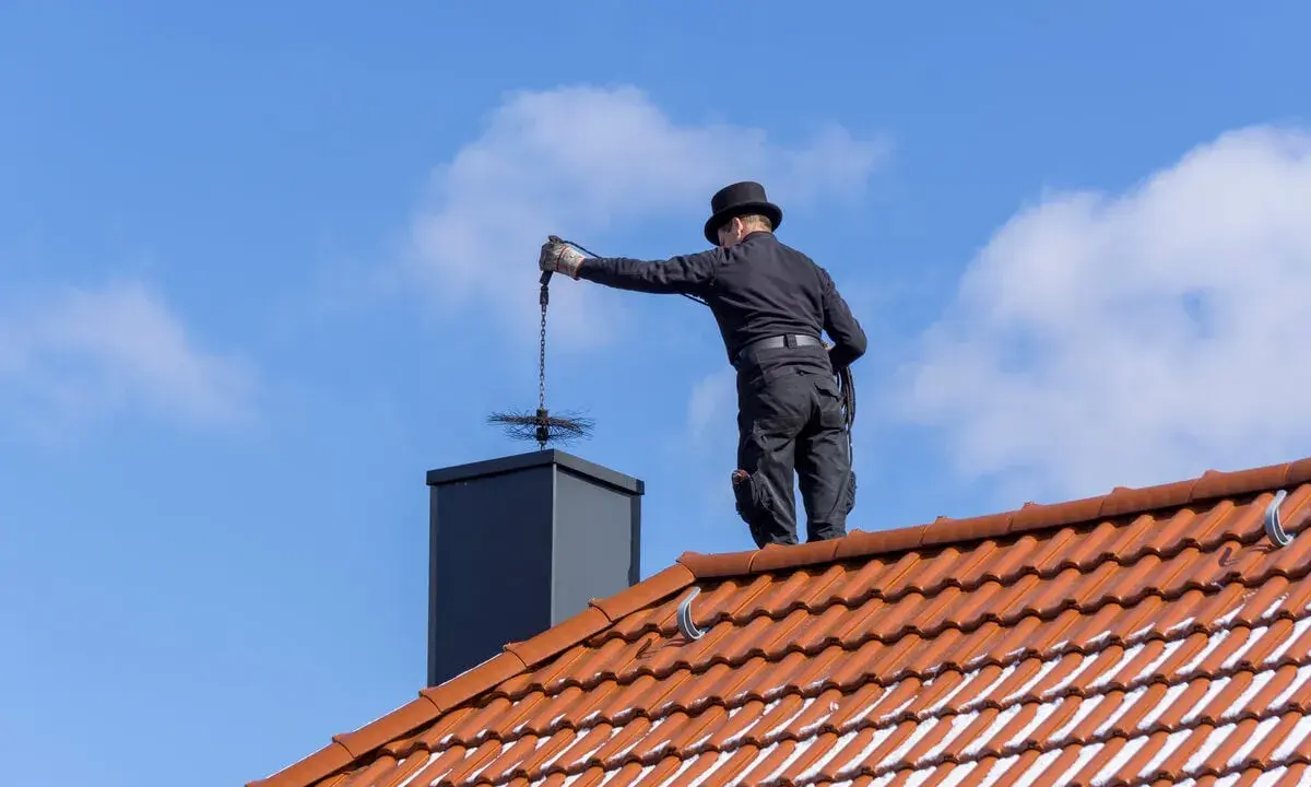 Deshollinador chimenea casero, con sombrero y traje negro, limpia la chimenea desde el tejado.
