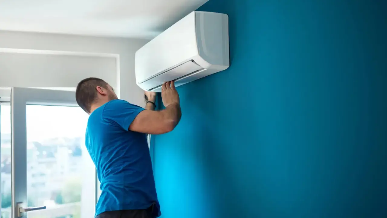 Hombre instalando aire acondicionado uno mismo en pared azul.