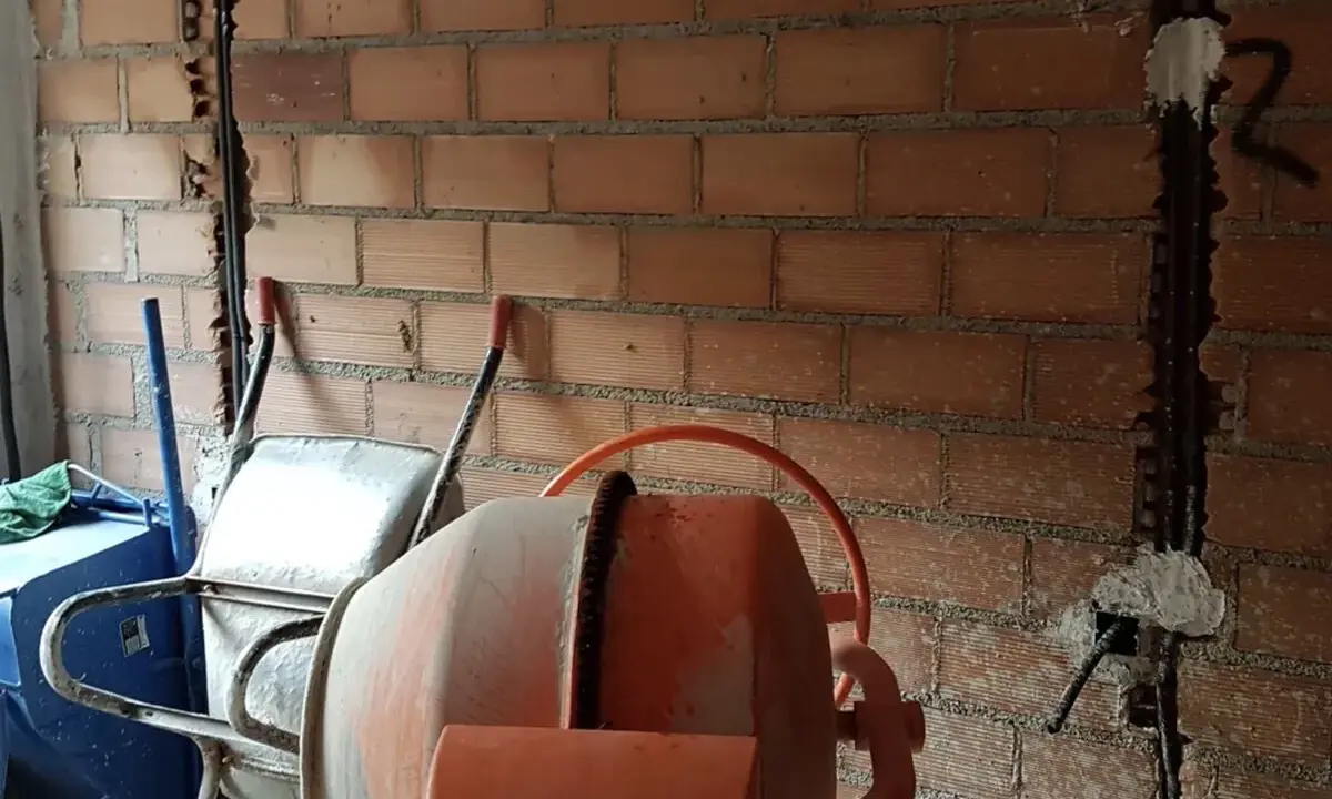 Preparativos para como tirar tabiques de ladrillo: carretilla, hormigonera y pared con ranuras para cables.