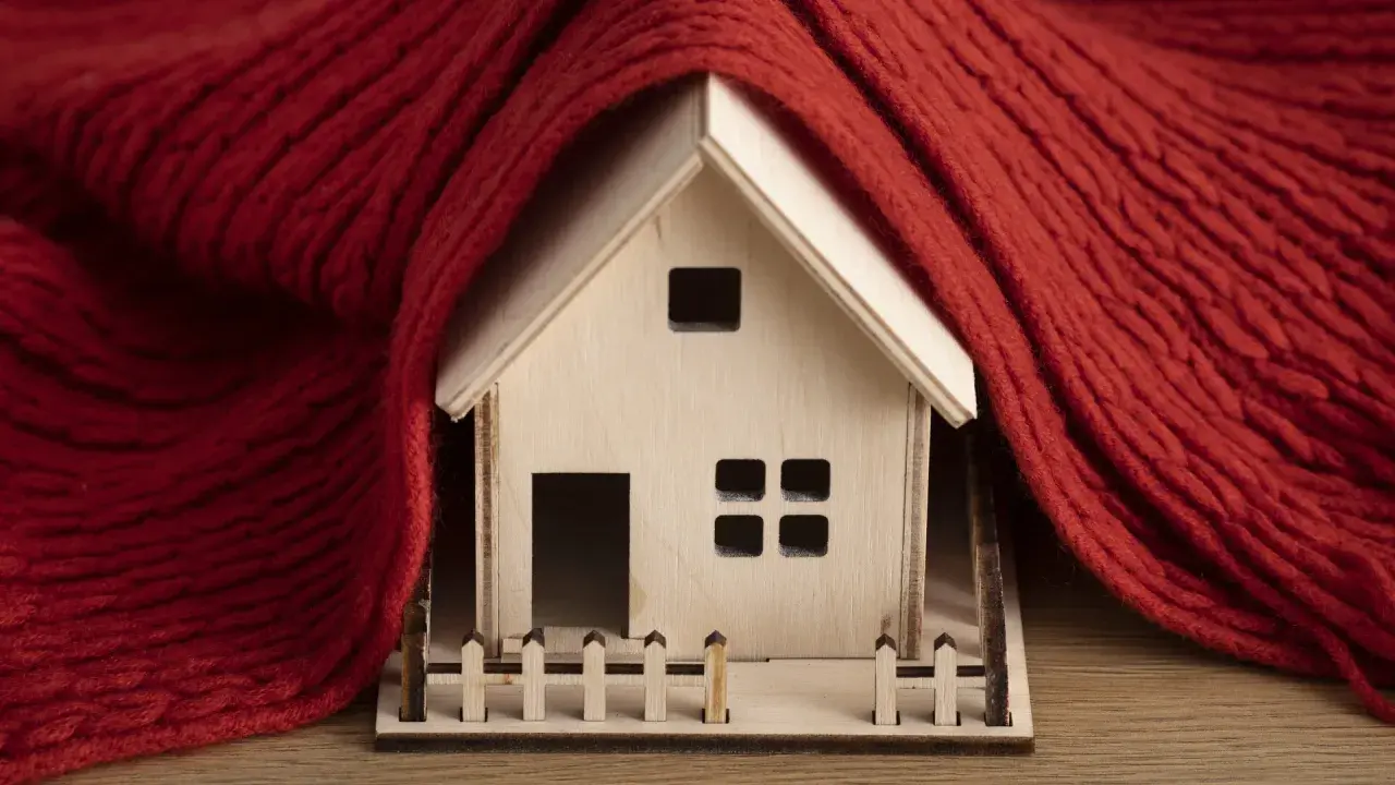 Casa de madera envuelta en manta roja, simbolizando la normativa de aislamiento térmico en viviendas para mantener el calor.