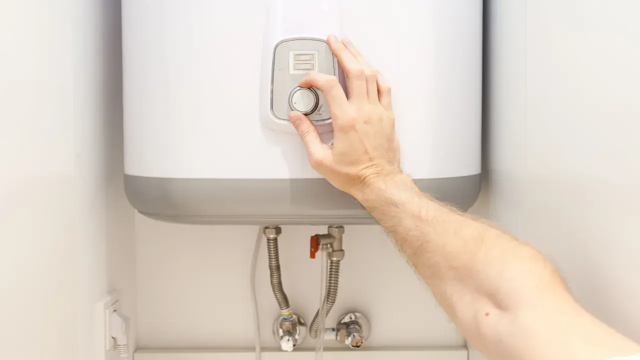 Mano ajustando el termostato de un termo eléctrico. Posiblemente para solucionar problemas de agua caliente.