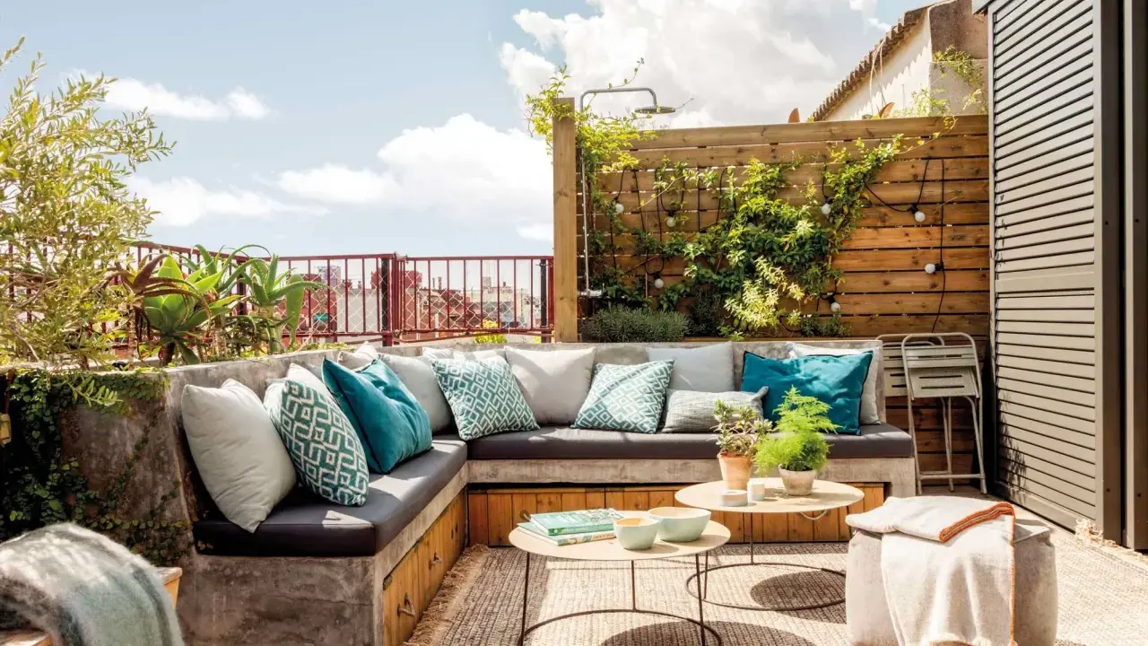 Un rincón perfecto para hacer una terraza: sofá de obra con cojines turquesas, mesas bajas y plantas.