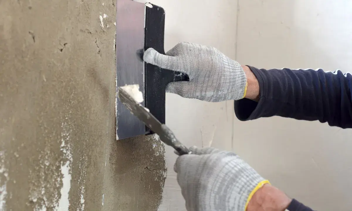 Manos enguantadas aplicando mortero para reparar pared.