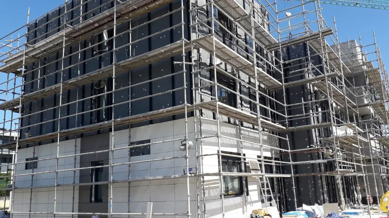 Edificio en construcción con andamios cubriendo la fachada. Se aprecian materiales de aislamiento y paneles, cumpliendo la ley de fachadas.