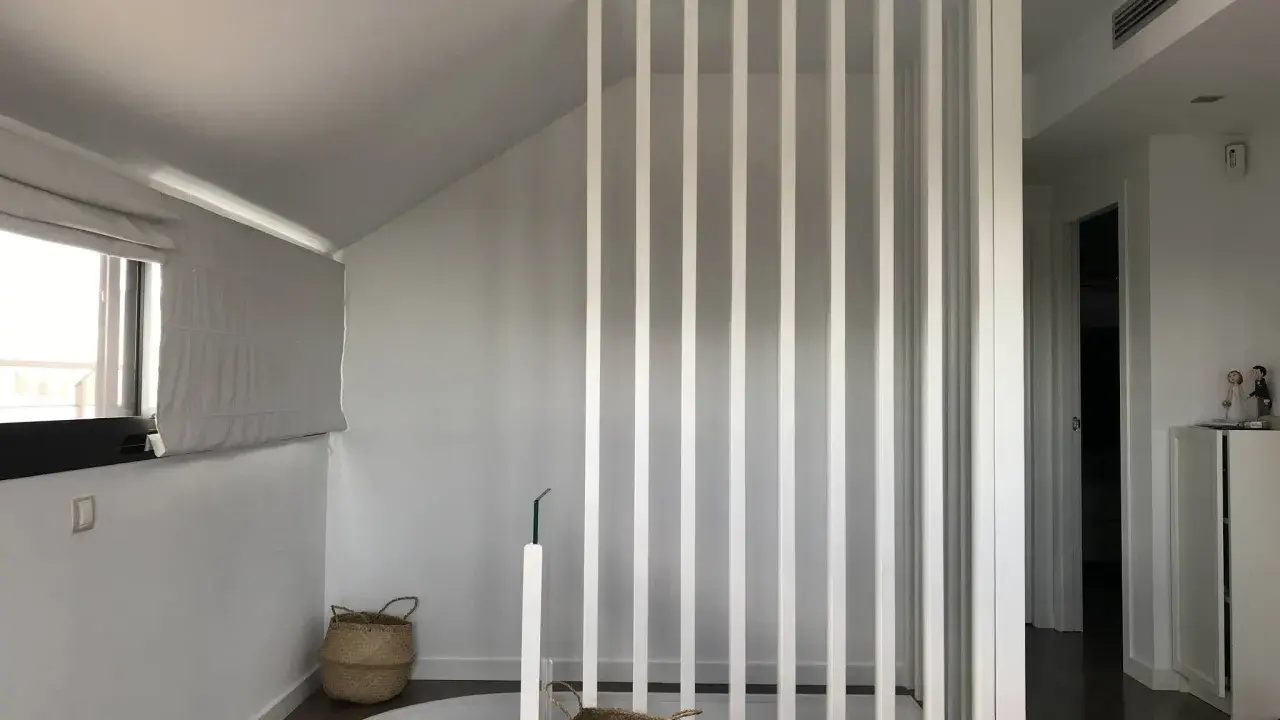 Modern interior with a white slatted divider, suggesting a design to tirar tabique para unir dos habitaciones. Baskets and a window add warmth.