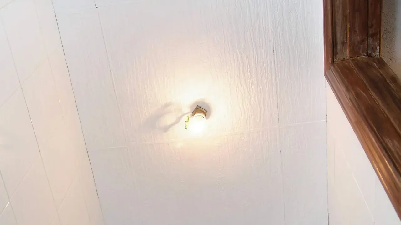 Techo con paneles de poliestireno extruido, una bombilla encendida y un marco de madera.