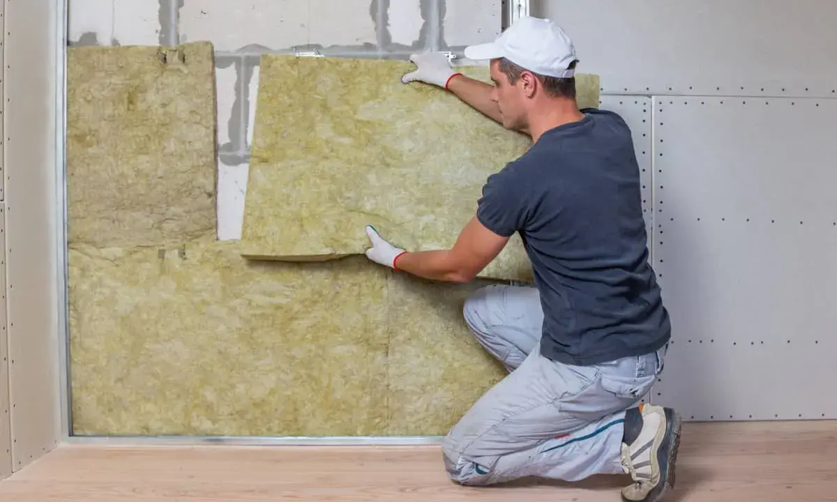 Hombre instalando aislamiento de lana de roca para como aislar una pared.