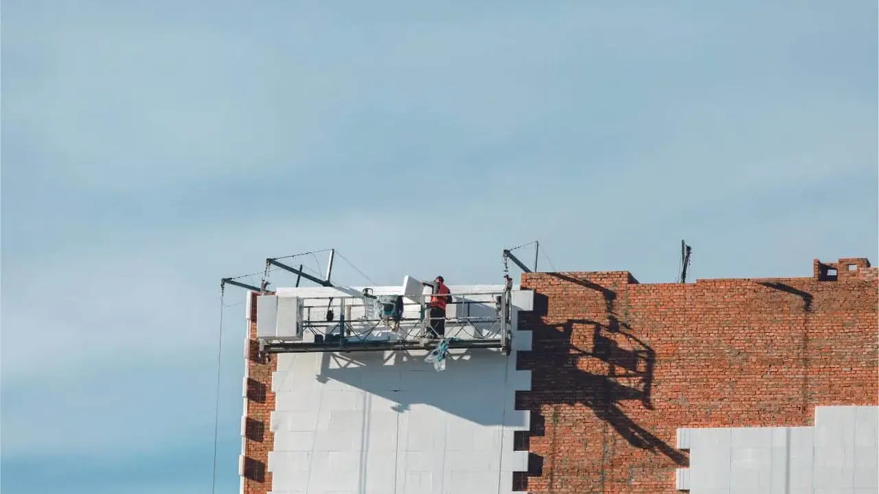 Trabajadores en una plataforma suspendida instalan paneles aislantes en un edificio, parte de un proyecto de sate.