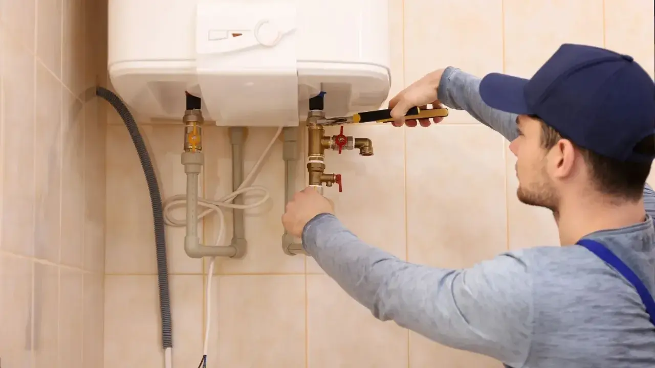 Un técnico ajusta las tuberías de un calentador de agua. Espera que la luz del termo no se apaga para confirmar que todo funciona bien.