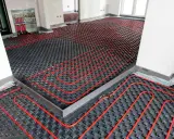 Instalación de un sistema de calefacción por suelo radiante enfria. Tubos rojos serpentean sobre paneles negros en una habitación en construcción.