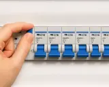 Mano manipulando un interruptor en un cuadro eléctrico, mostrando varios disyuntores. Esto ilustra qué es un diferencial eléctrico y su función de protección.