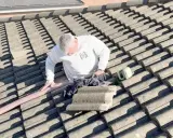 Hombre en tejado trabajando en el aislamiento térmico del tejado. Se ve una manguera rosa y una herramienta verde.