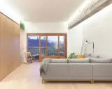 Salón moderno con sofá gris, grandes ventanales y **techos con vigas de hormigón decorar** el espacio con estilo industrial.