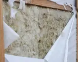 Aislamiento de lana de roca expuesto, con una barrera de vapor blanca rasgada que revela la textura fibrosa.