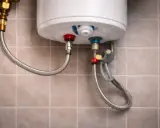 Detalle de conexiones de un termo eléctrico. Se observa una manguera flexible conectada a la válvula de seguridad, indicando que el termo eléctrico gotea por ahí.