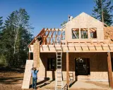 Obreros trabajan en la estructura de madera de una casa, mostrando los pasos a seguir para construir una casa.