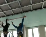Dos trabajadores instalan placas de yeso para como aislar un techo por el interior. Se ve la estructura metálica del falso techo.