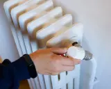 Mano ajustando el termostato de un radiador, parte de los contadores individuales de calefacción central.