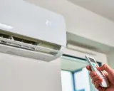 Mano ajustando el control remoto de un aire acondicionado para que gasta menos. La pantalla muestra 21 grados.