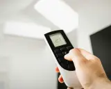 Mano ajustando el mando de aire acondicionado a 21 grados. Instrucciones claras para un confort óptimo.