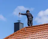 Deshollinador chimenea casero, con sombrero y traje negro, limpia la chimenea desde el tejado.