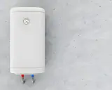 Termo eléctrico blanco colgado en pared de cemento. Las tuberías de agua fría y caliente indican que el termostato podría estar fallando porque salta el termostato del termo eléctrico.