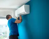 Hombre instalando aire acondicionado uno mismo en pared azul.