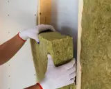 Manos enguantadas colocan aislamiento de lana de roca para saber como aislar termicamente una habitacion.