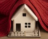 Casa de madera envuelta en manta roja, simbolizando la normativa de aislamiento térmico en viviendas para mantener el calor.