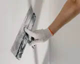 Mano enguantada aplicando yeso a una pared, parte del proceso de como alicatar una pared exterior.