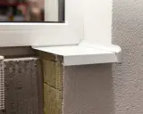 Detalle constructivo de un alféizar blanco sobre aislamiento y mampostería, con malla de refuerzo visible.