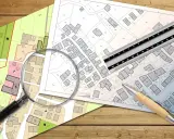 Planos de parcelas con lupa, regla y bolígrafo. Se analiza la diferencia entre edificabilidad y ocupación en urbanismo.