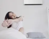 Mujer estirándose en la cama bajo el aire acondicionado, ideal para saber como poner el aire acondicionado para dormir y disfrutar de un descanso fresco.