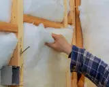 Mano colocando aislamiento en la pared de madera. Mejora el aislamiento de edificios para mayor eficiencia energética.