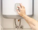 Mano ajustando el termostato de un termo eléctrico. Posiblemente para solucionar problemas de agua caliente.