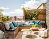 Un rincón perfecto para hacer una terraza: sofá de obra con cojines turquesas, mesas bajas y plantas.